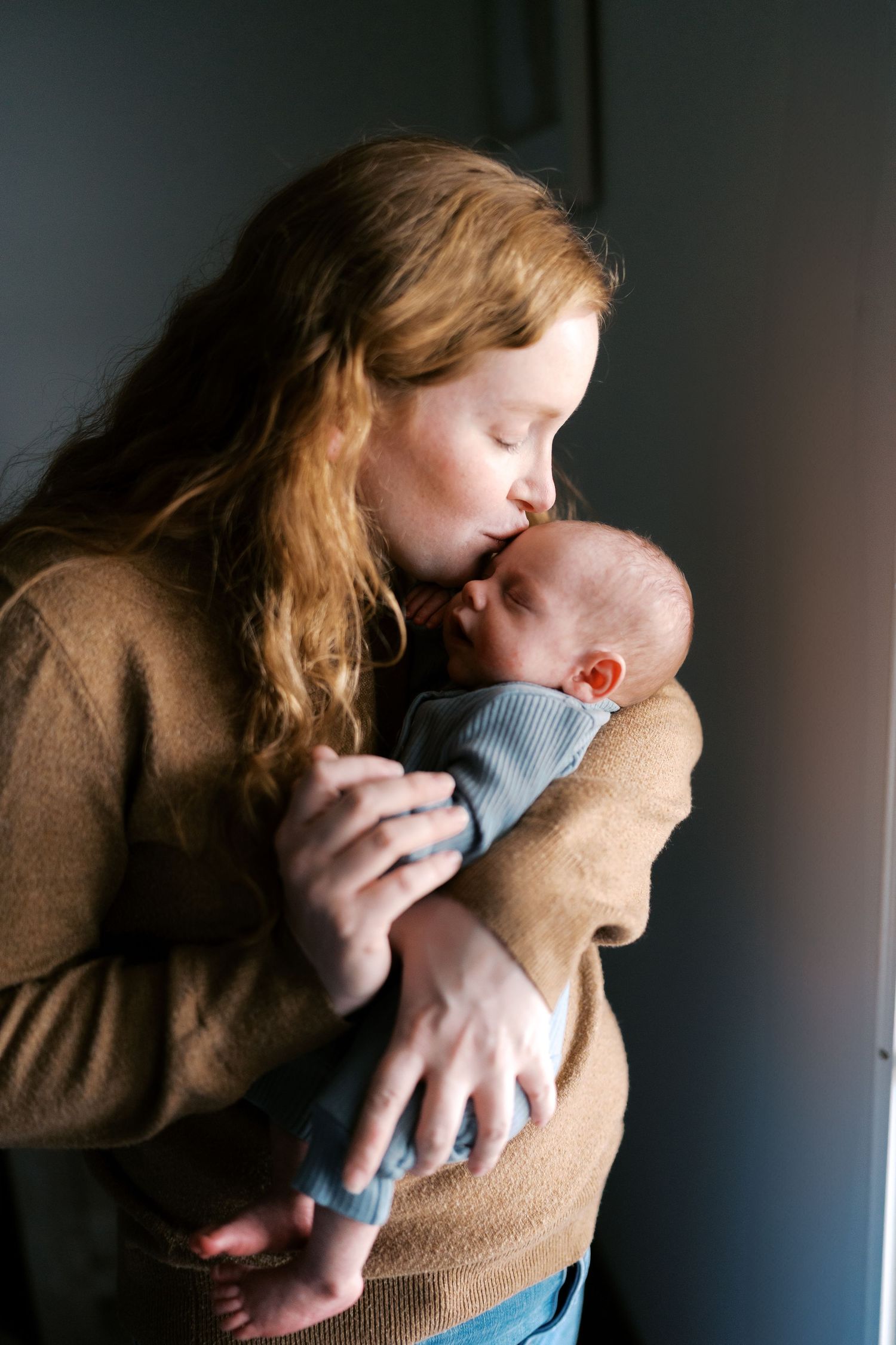 Loving interaction between parent and infant in moody indoor lighting.