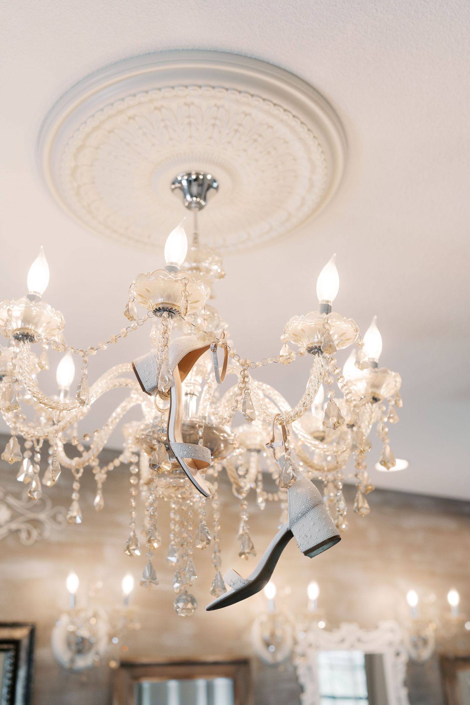 Crystal chandelier with hanging bridal shoes in elegant wedding venue.