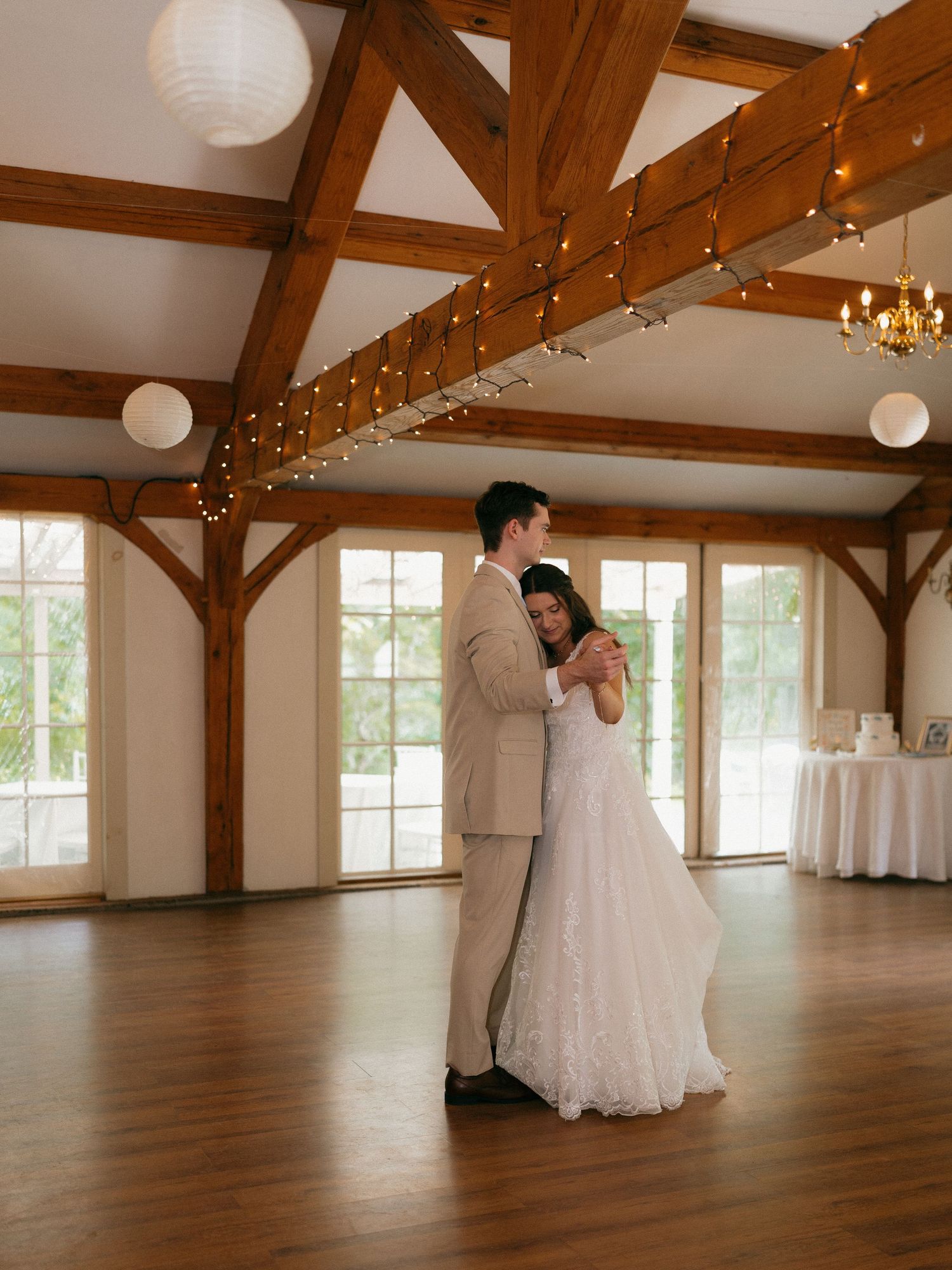 Newlyweds share an intimate dance in a rustic venue with exposed beams and natural light.
