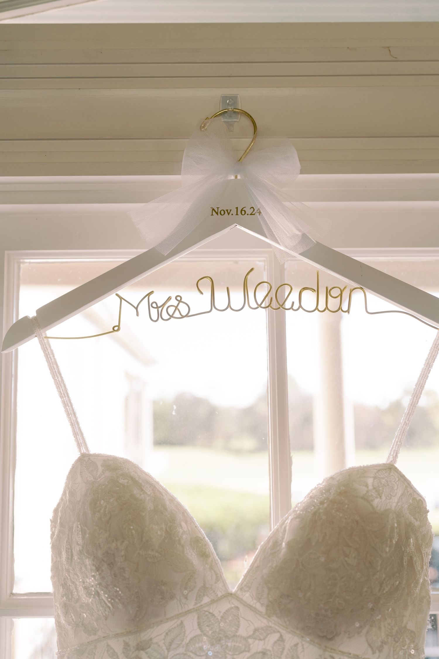 Personalized wedding dress hanger with bride's name displayed against window light.