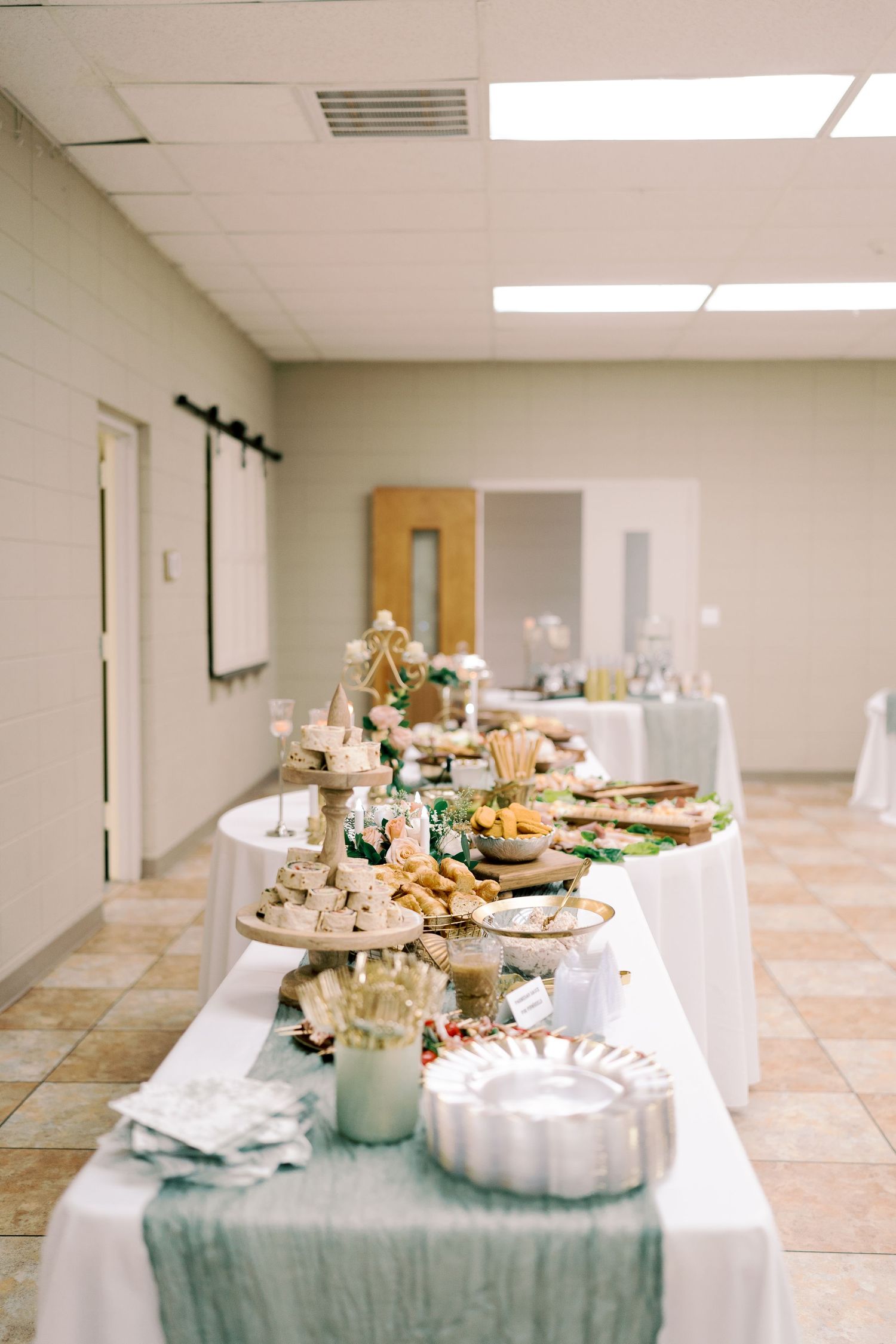 Elegant wedding reception buffet table with white linens and various appetizers and desserts.