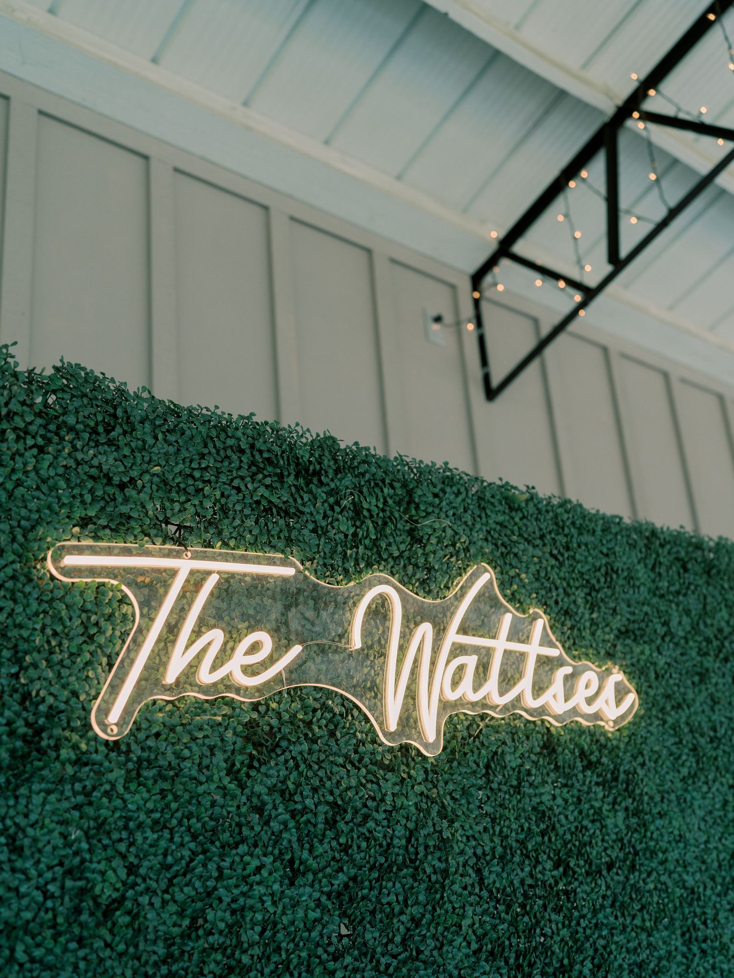 Illuminated neon wedding sign mounted on green foliage wall.