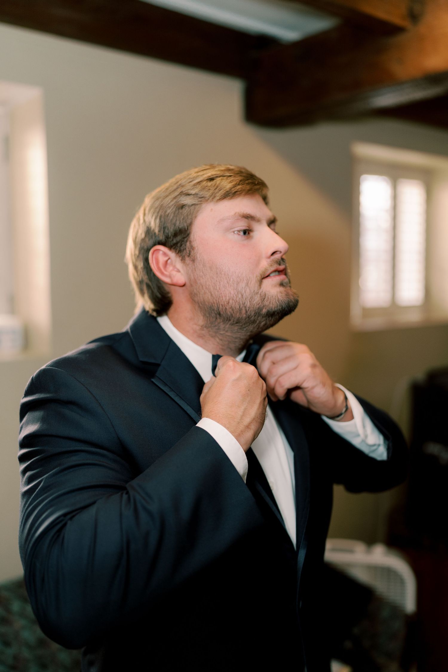Pre-ceremony preparation with formal attire adjustment in dimly lit room.