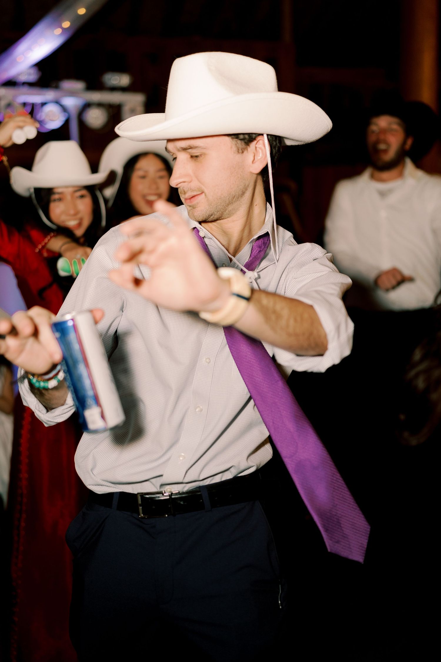 Person in grey suit with purple tie and white cowboy hat dancing at an event.