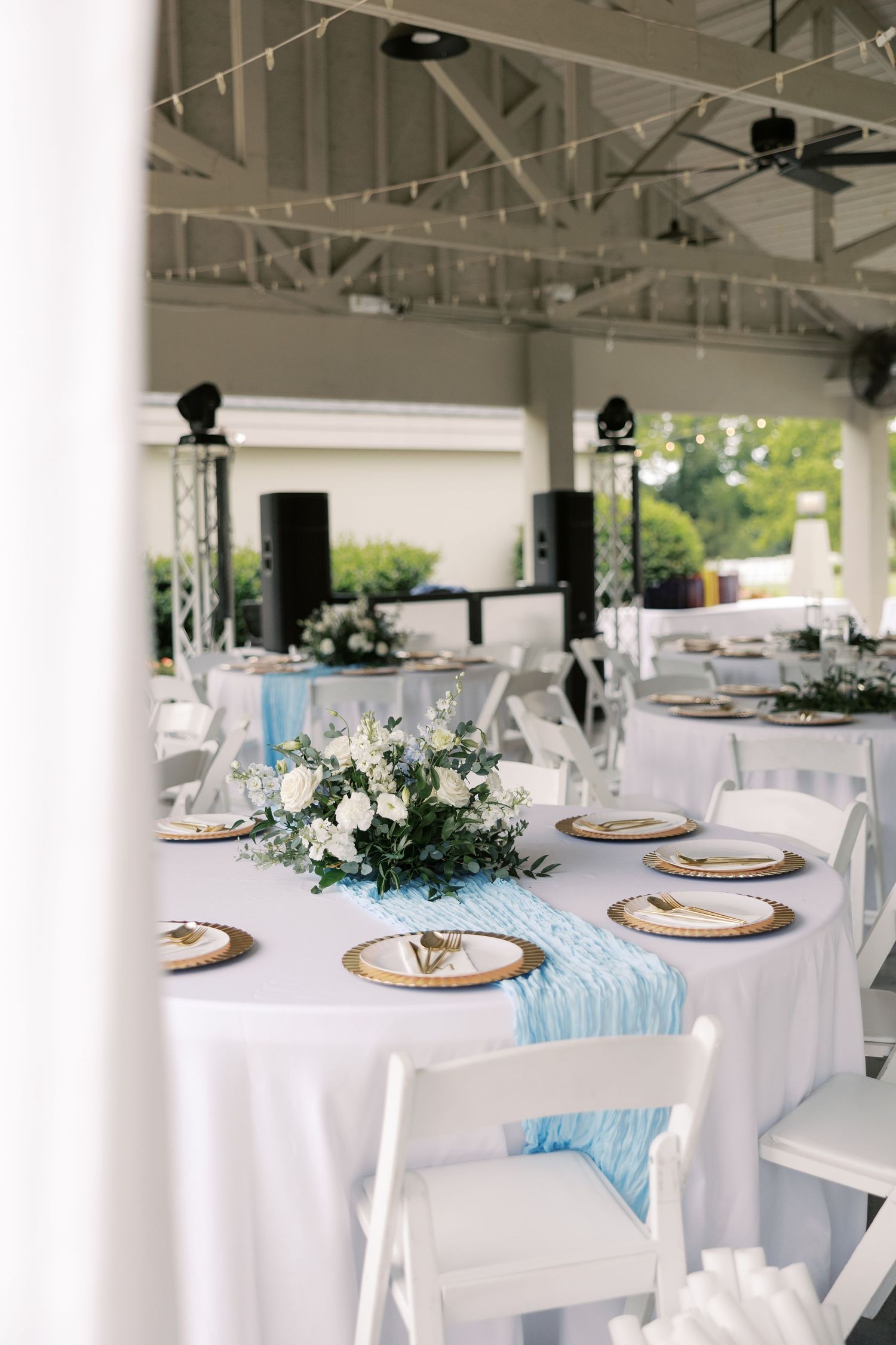 Wedding reception venue with white tablecloths, light blue accents, and gold charger plates.