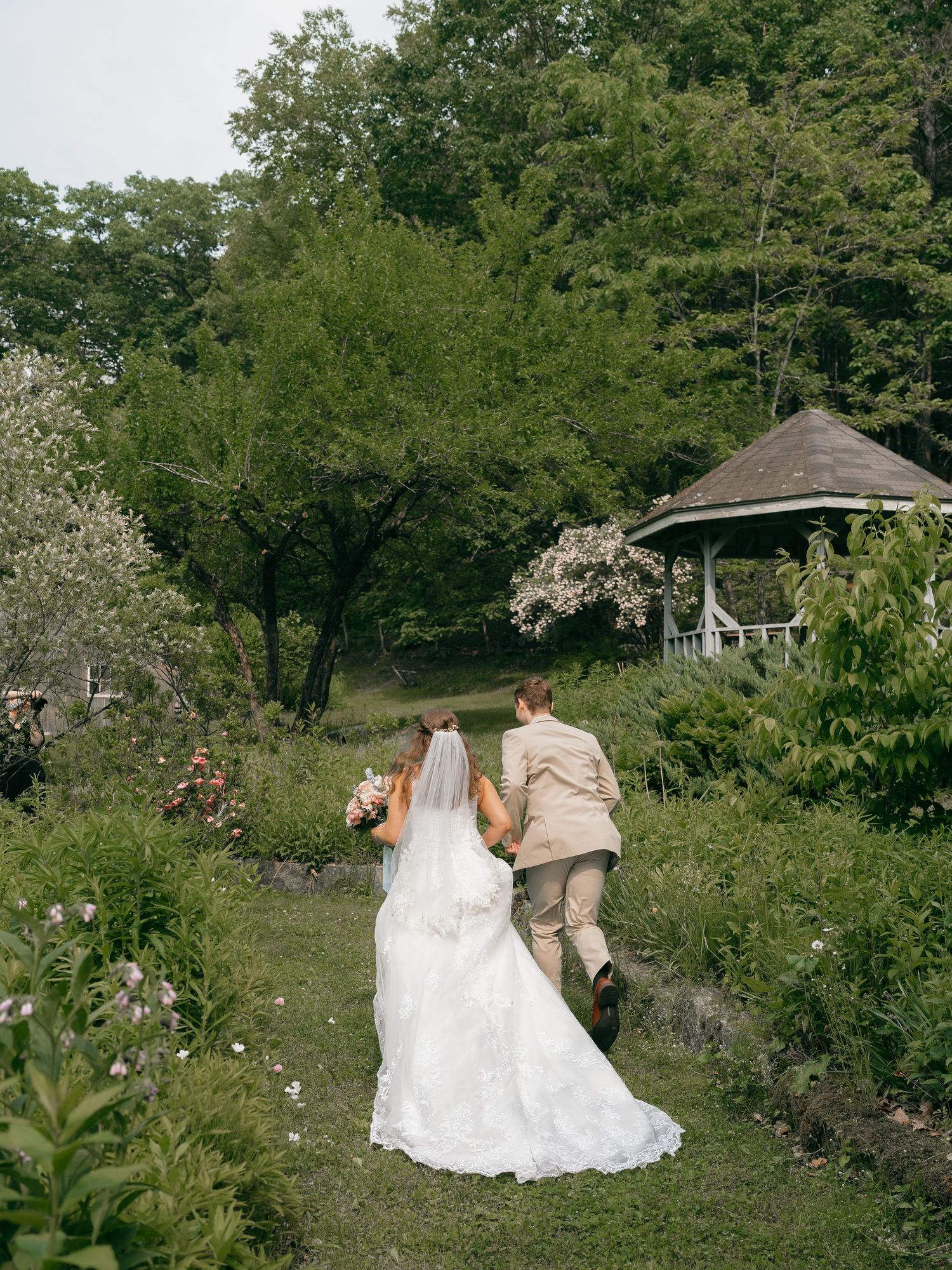 Couple walking through garden path towards gazebo on wedding day.