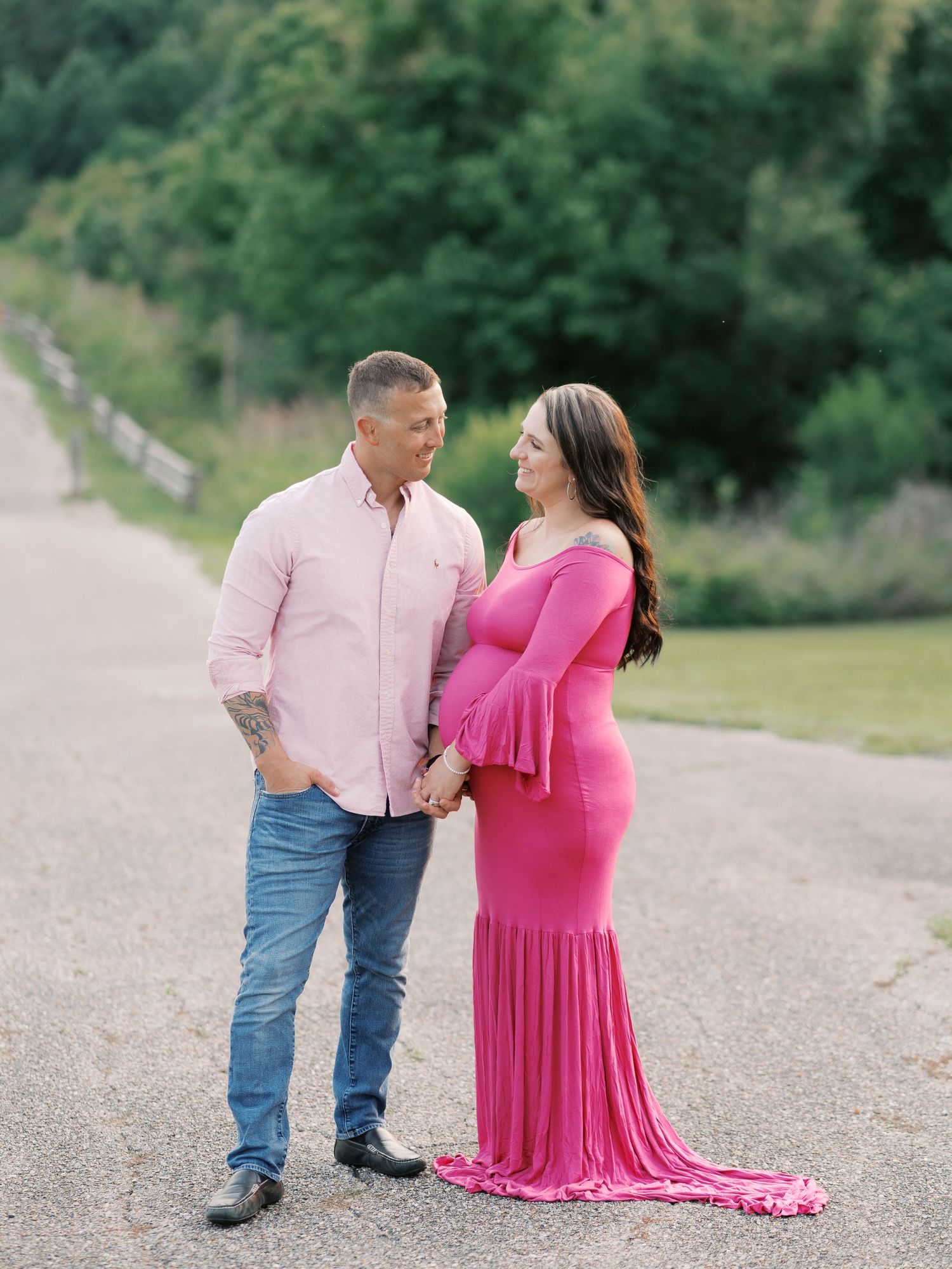 Couple in pink outfits sharing intimate moments during outdoor maternity photoshoot.