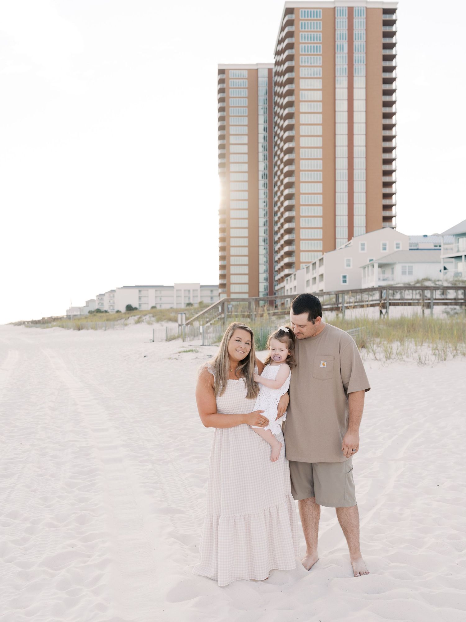 Family members walking on beach sand with tall coastal apartment buildings in the background.