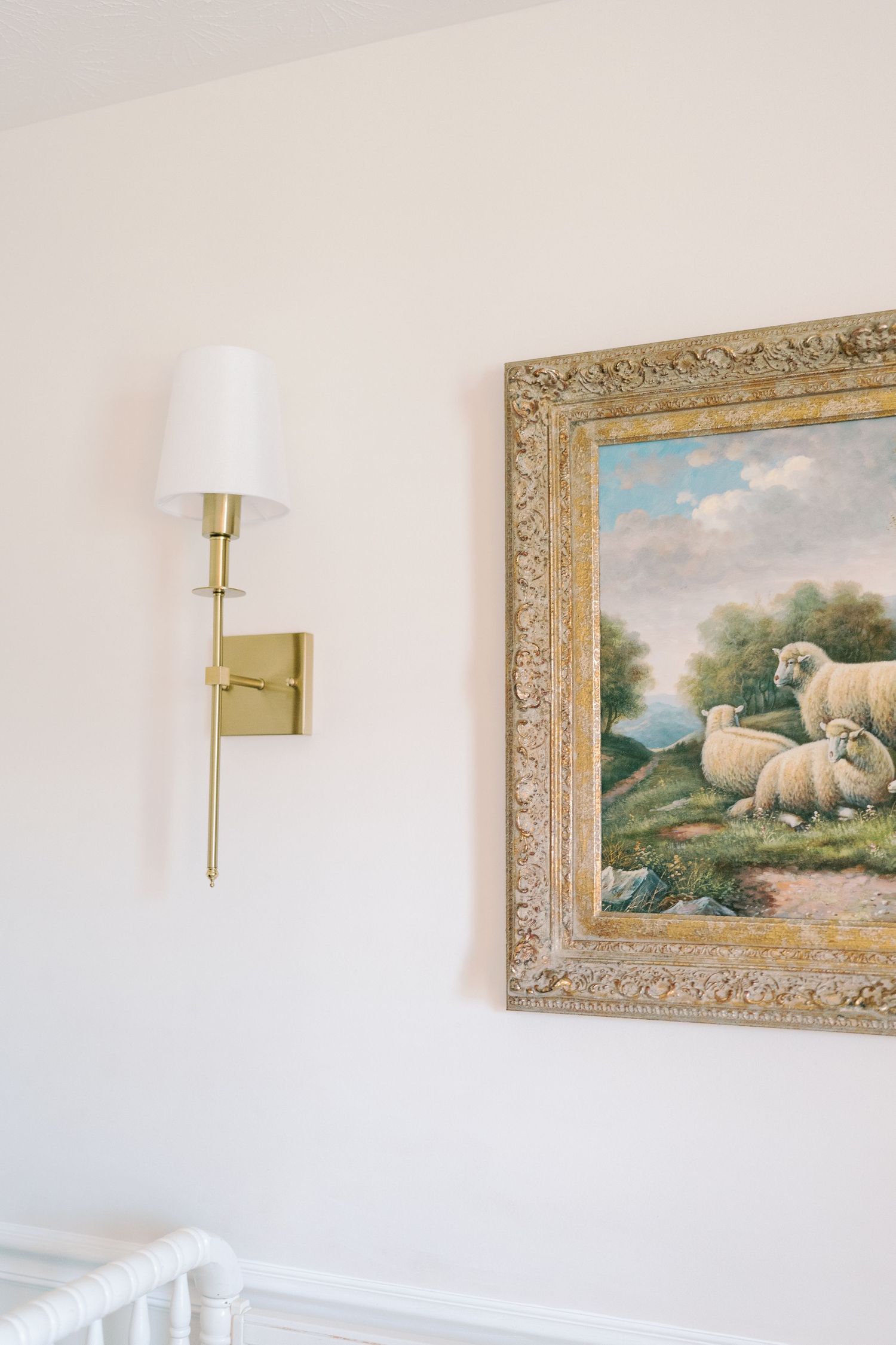 Pastoral landscape paintings in ornate gold frames hang above white wainscoting.