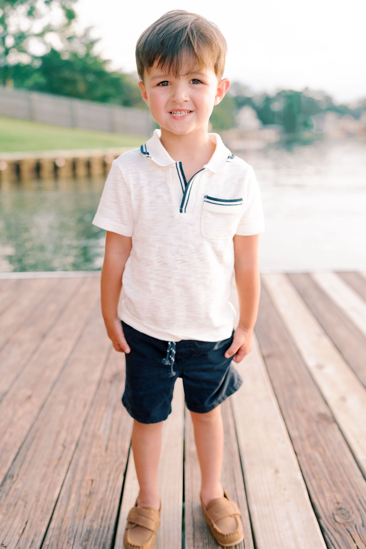Child in nautical outfit poses on wooden dock by the water.