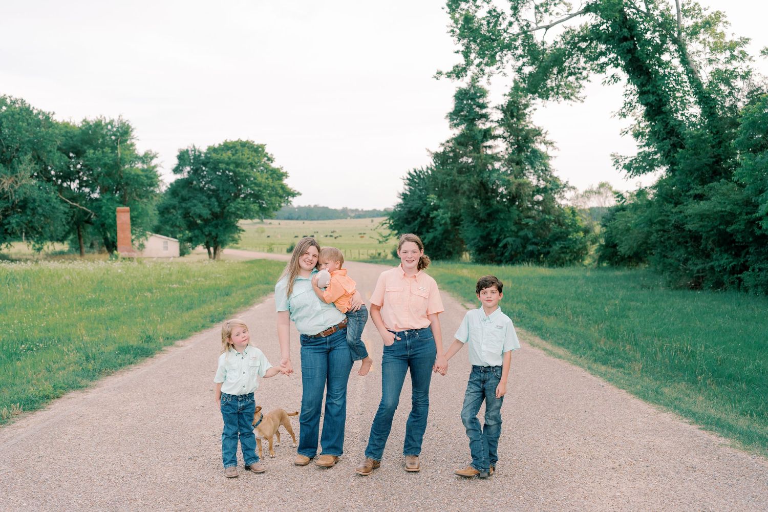 Family walking together on a rural path surrounded by green fields and trees.