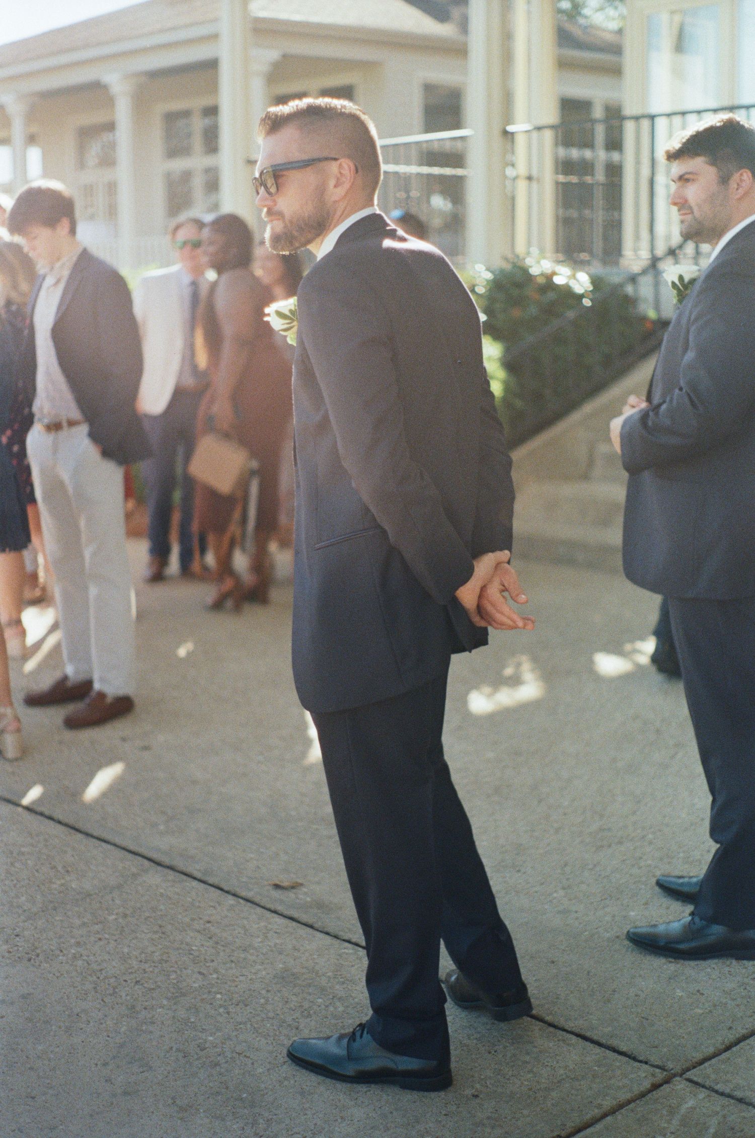 Formal event guests in suits and dresses gathered outside venue.
