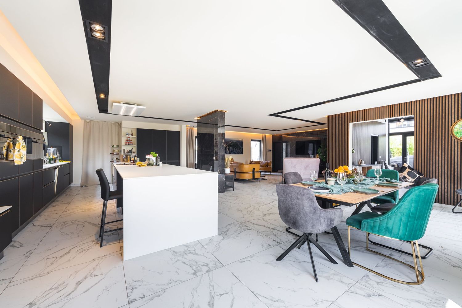 Luxurious open-plan kitchen and dining area with marble floors, dark cabinetry, and colorful velvet dining chairs.
