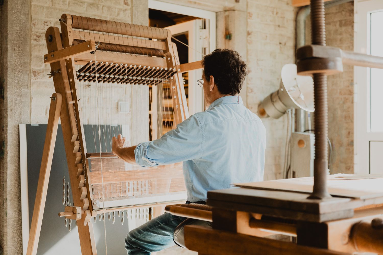 A craftsman weaving fabric on a traditional wooden loom in a bright artisan workshop.
