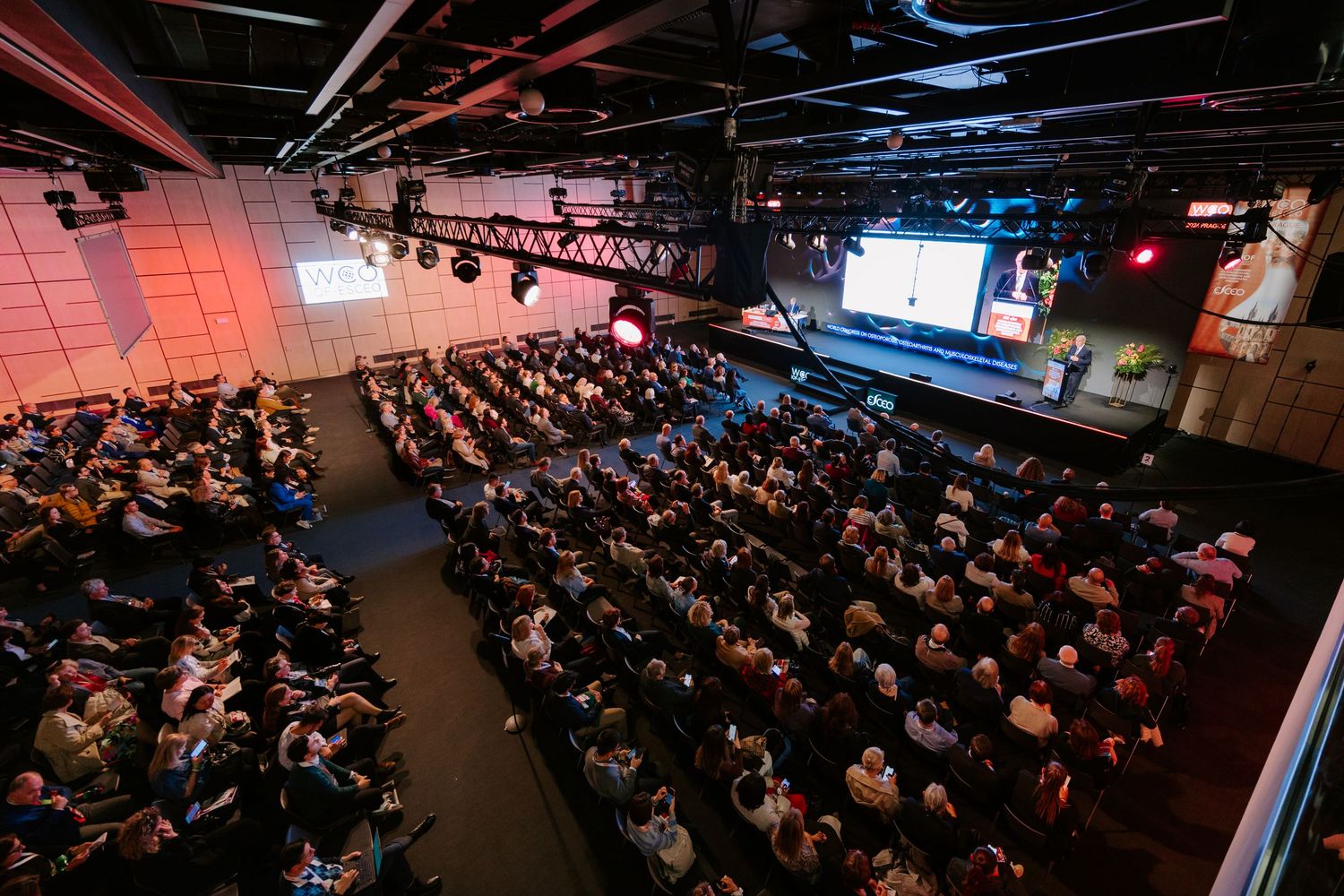 A large audience fills a modern conference hall with stage lighting and presentation screens at a tech event.