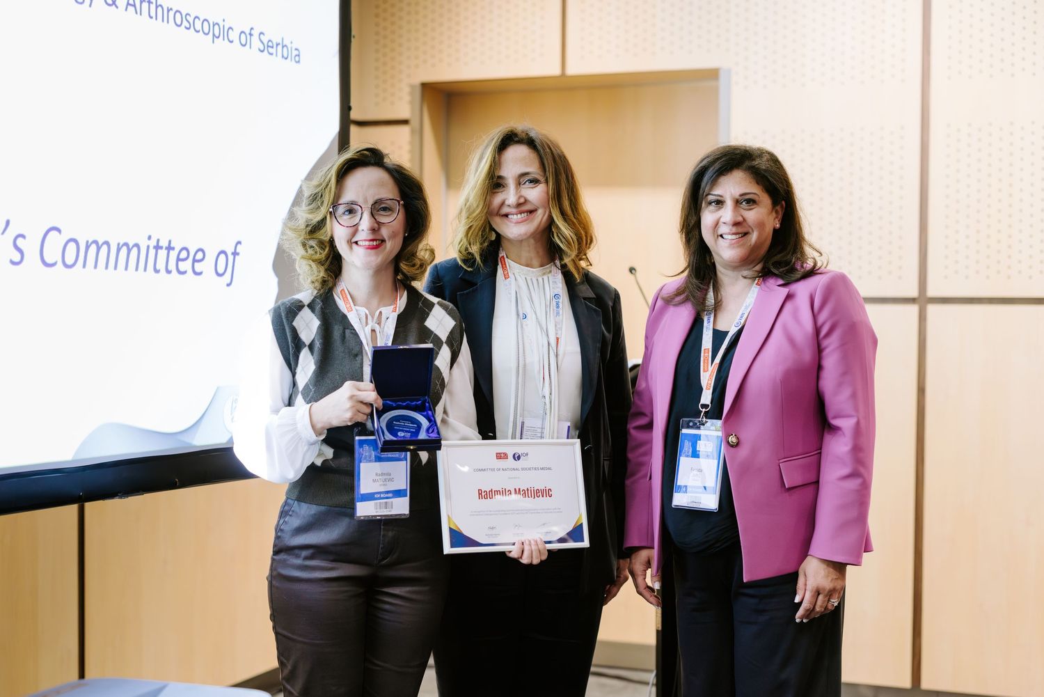 Three women pose together at an arthroscopic surgery conference, with one holding an award certificate and another displaying a medal.