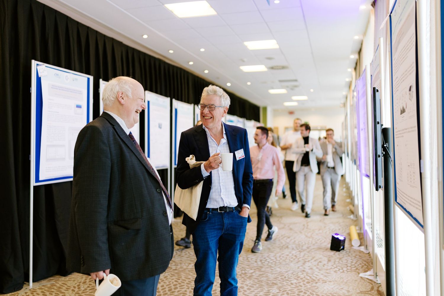 Two professionals discussing research posters at an academic conference event in a modern venue.
