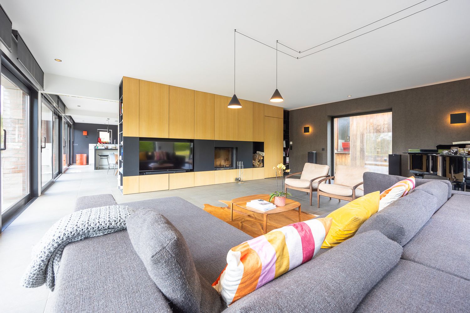 Spacious modern living room with gray sofa, yellow cabinetry, fireplace, and floor-to-ceiling windows.
