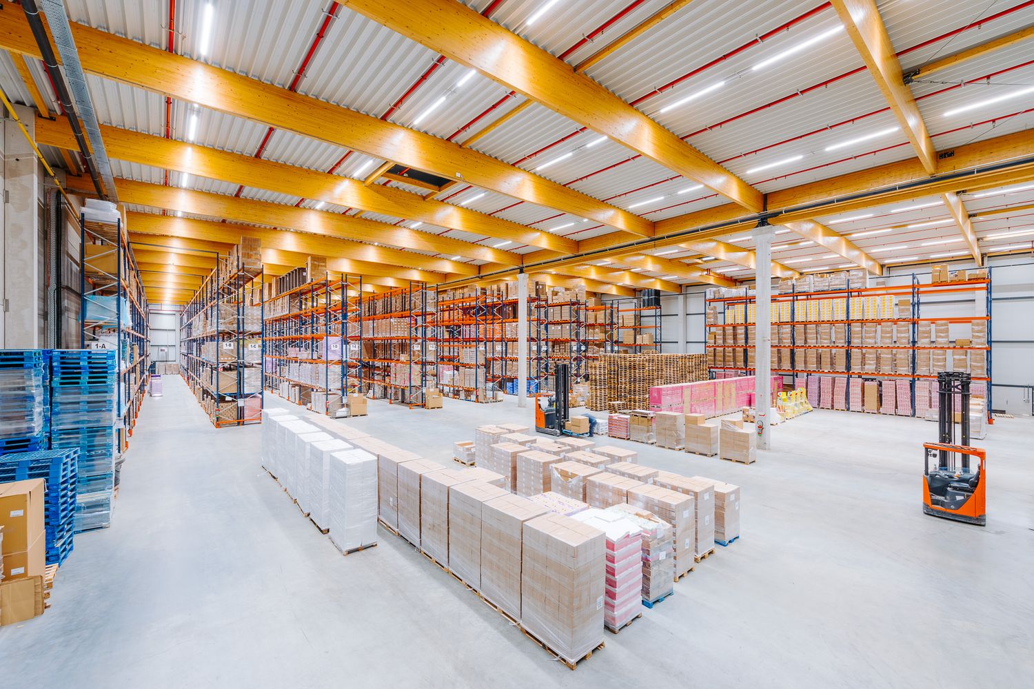 Spacious industrial warehouse interior with tall yellow shelving racks filled with stacked goods.