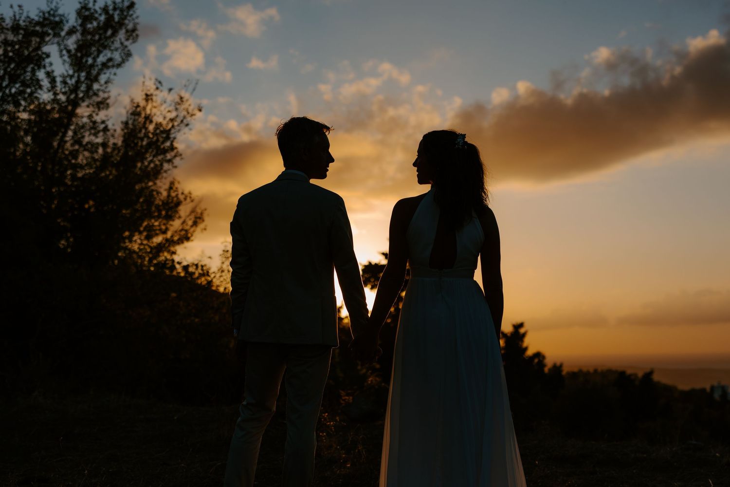 Romantic silhouette of a couple holding hands against a stunning golden sunset sky.