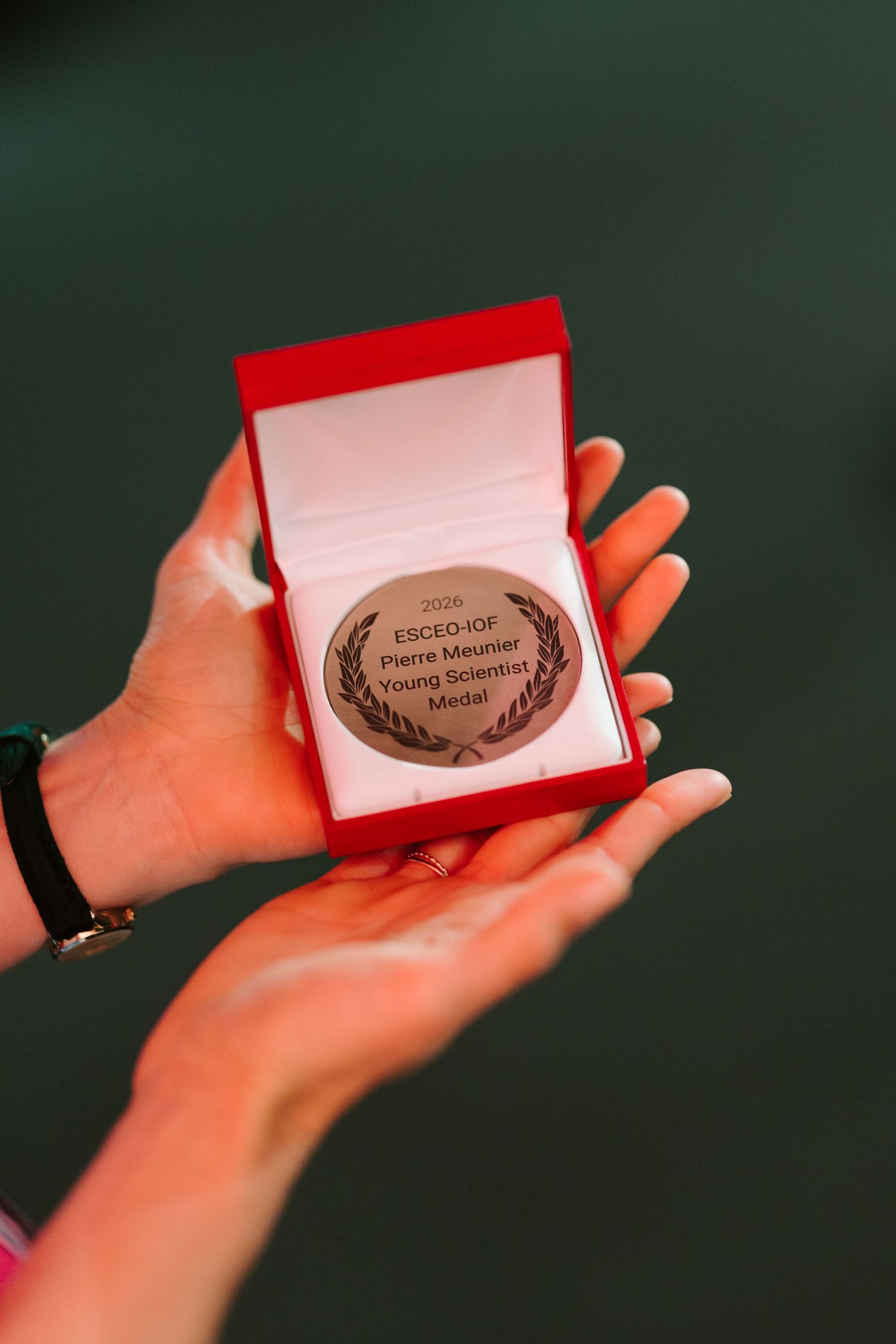 Hands holding a red box with the ESCEO-IOF Pierre Meunier Young Scientist Medal inside.
