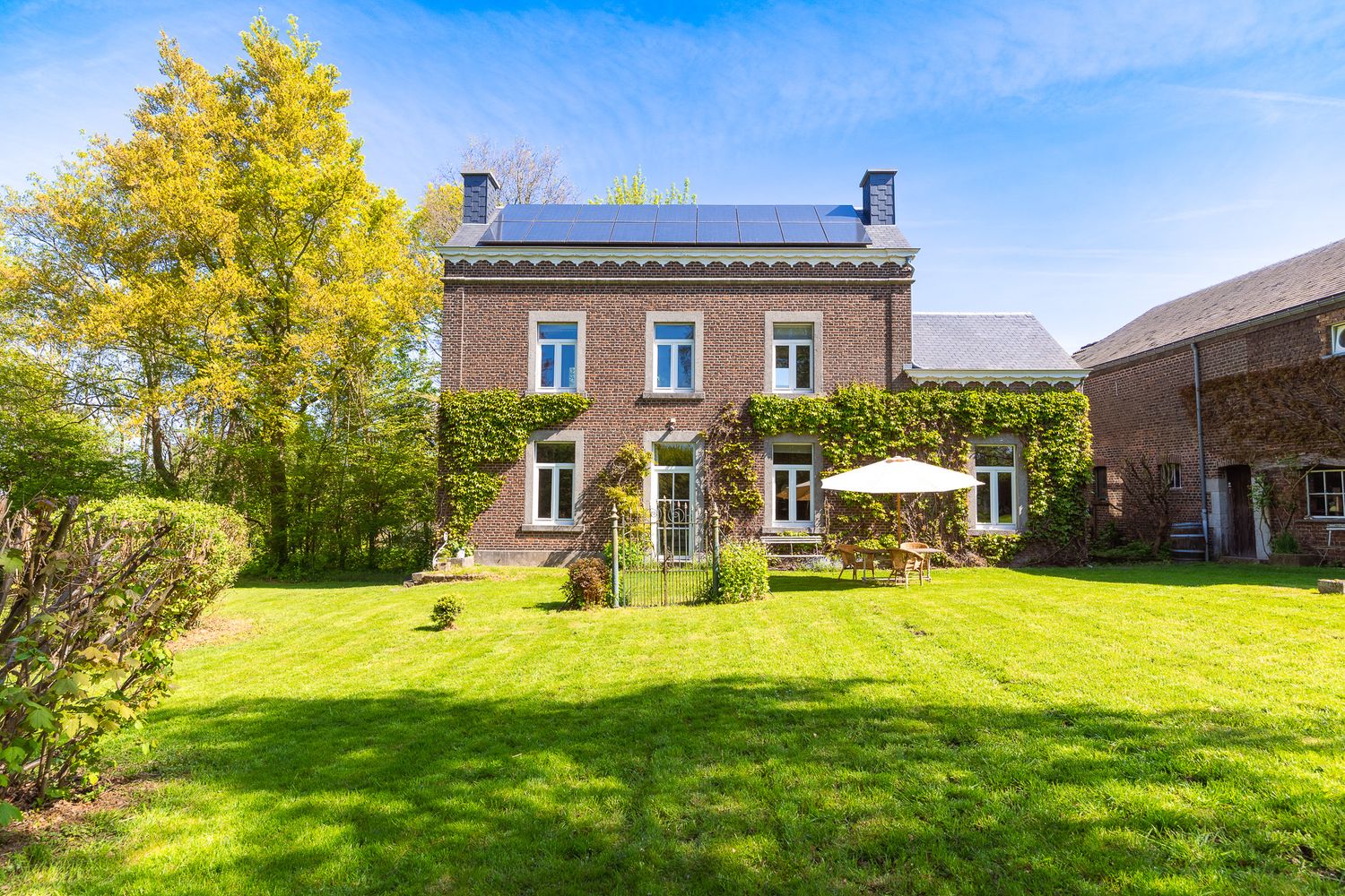 Charming ivy-covered brick manor house with solar panels and a well-maintained garden.