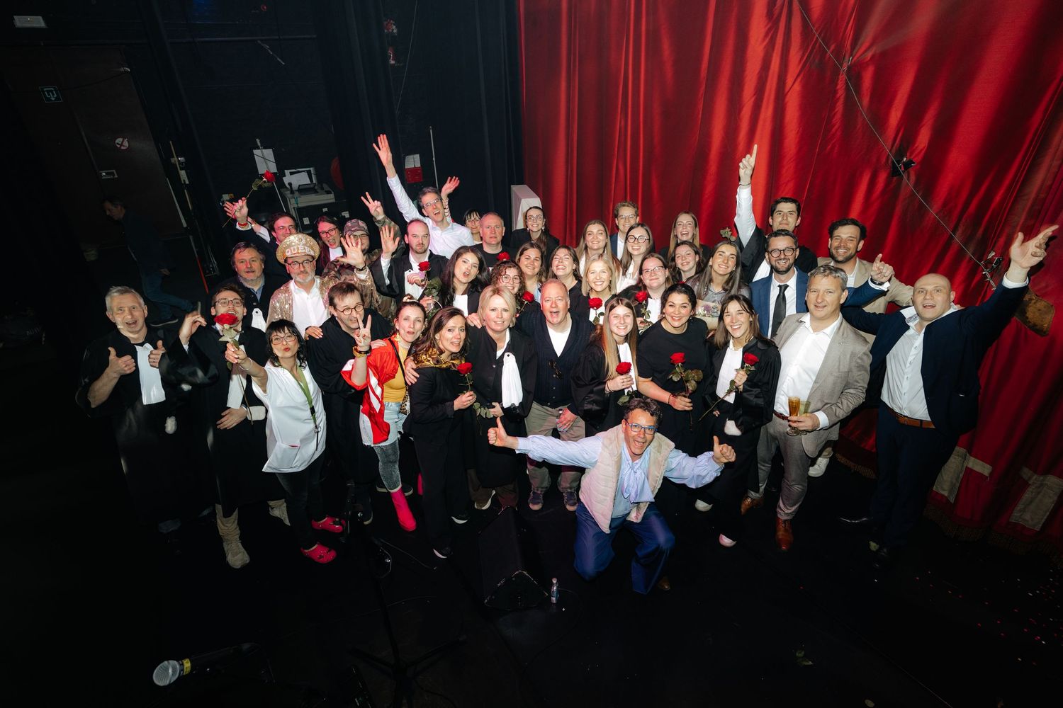 Large group photo of smiling event attendees celebrating in front of red stage curtain.