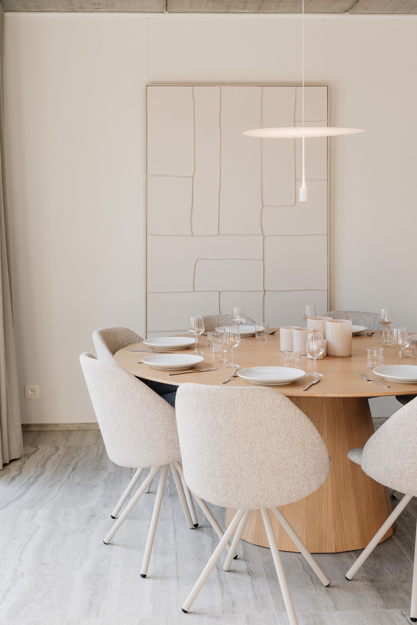 Minimalist dining room with oval wood table, cream bouclé chairs, pendant light, and abstract wall art in neutral tones.