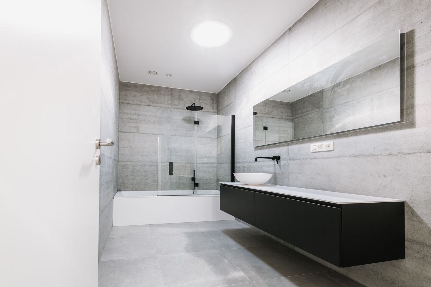 Minimalist bathroom with gray tiles, black fixtures, floating vanity, and combined shower and bathtub.