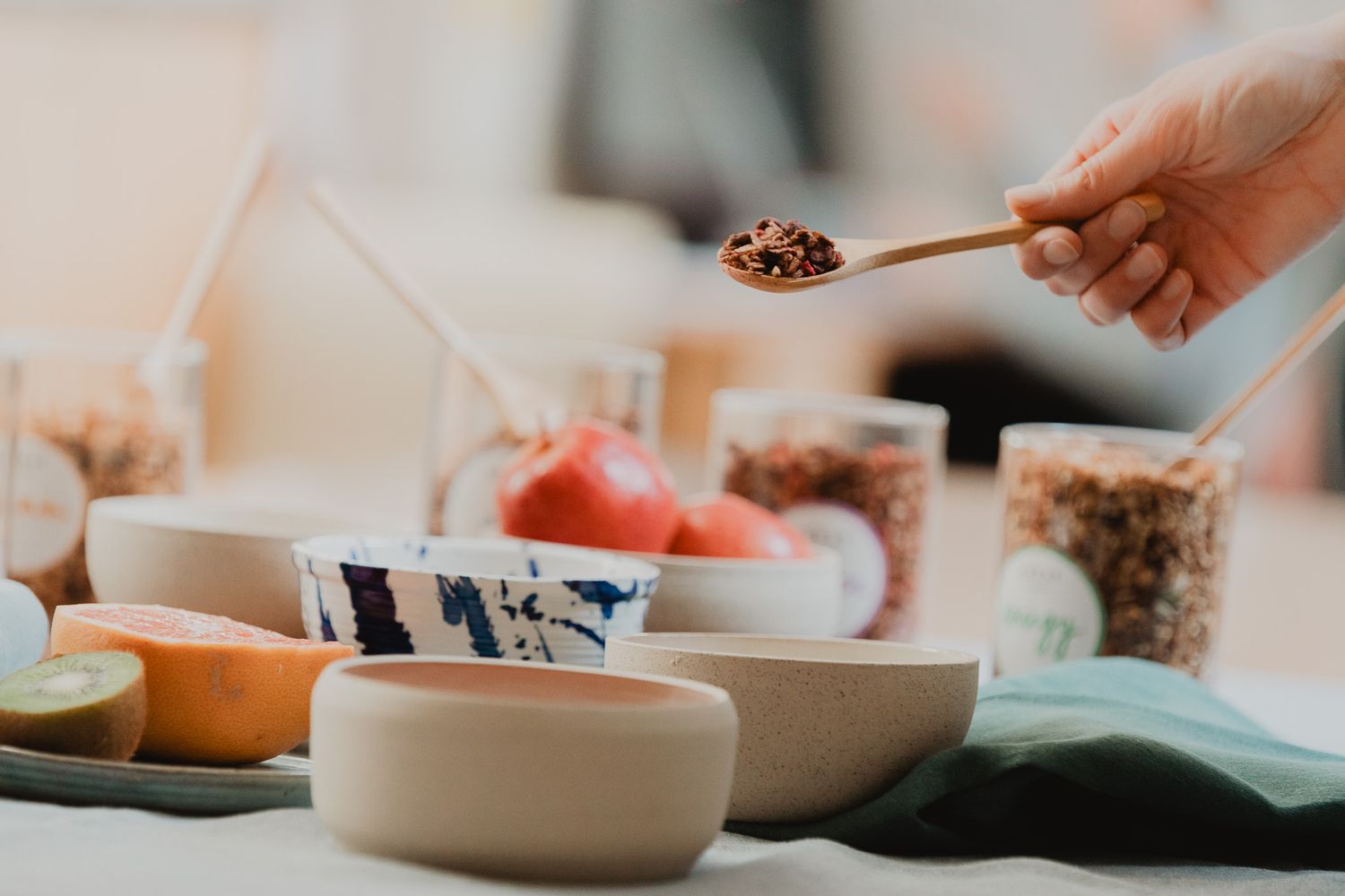 Hand holding a wooden spoon with spices over ceramic bowls of healthy food ingredients.