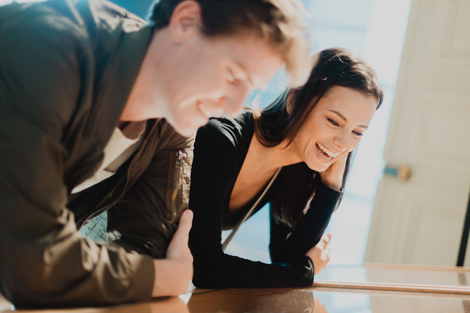 A man and woman smiling and leaning over a table in a warm sunlit setting.