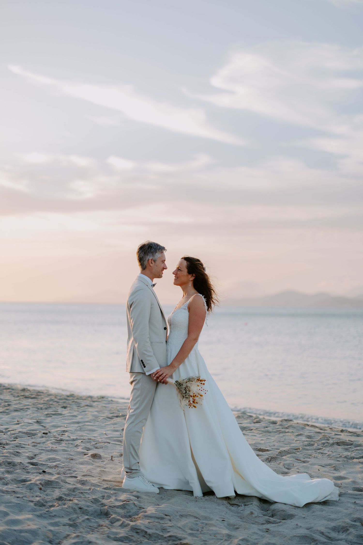Bride and groom holding hands on a sandy beach at sunset during their romantic wedding ceremony.