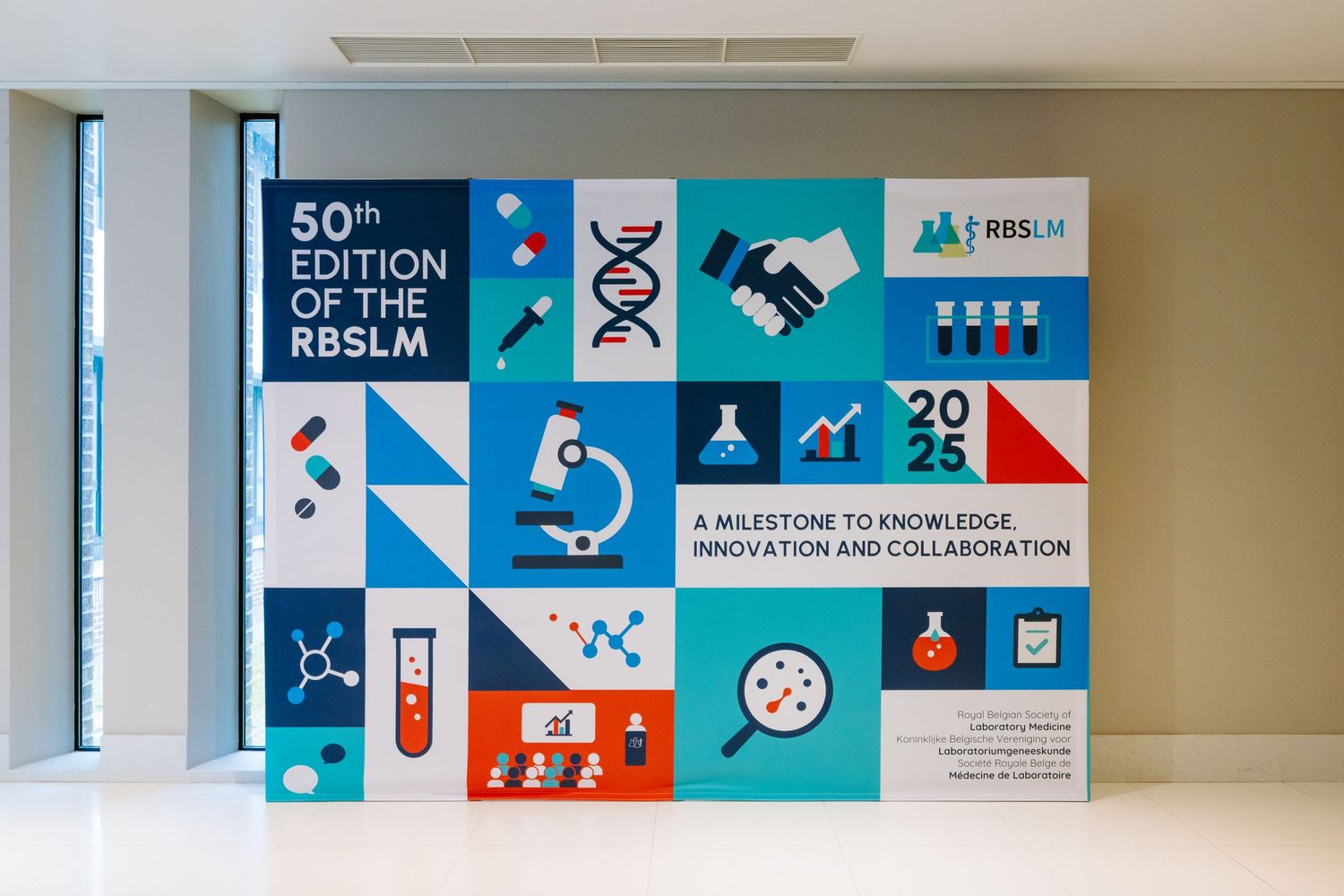 Wall display celebrating the 50th edition of RBSLM 2025, featuring science icons, DNA helix, and innovation collaboration theme.
