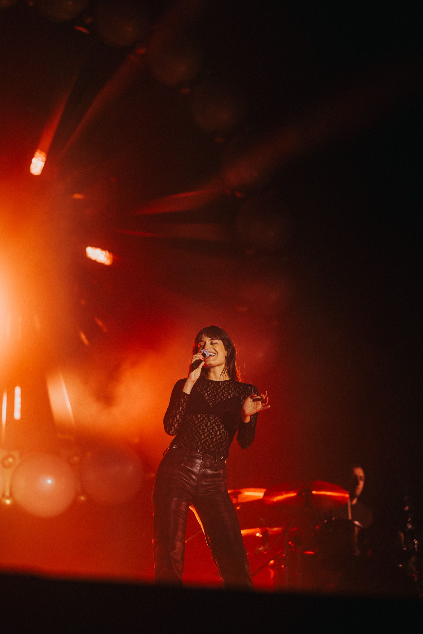 Female singer performing on stage with dramatic red lighting and smoke effects at a live concert.