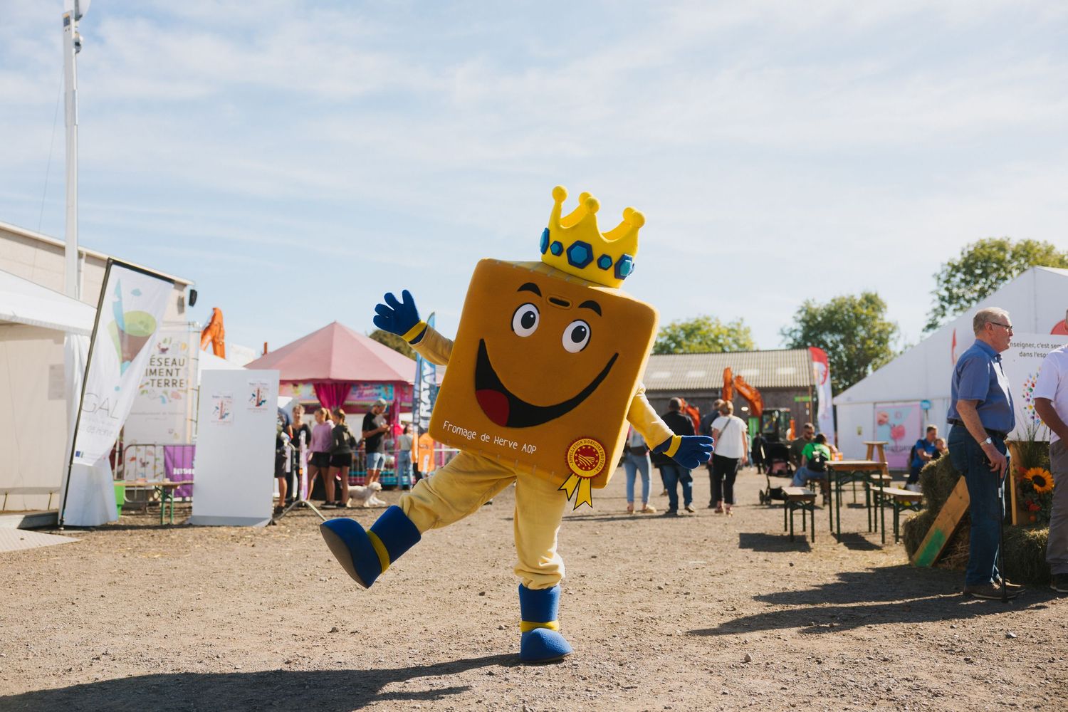 Cheerful golden crown mascot character dancing at outdoor festival fairground event.