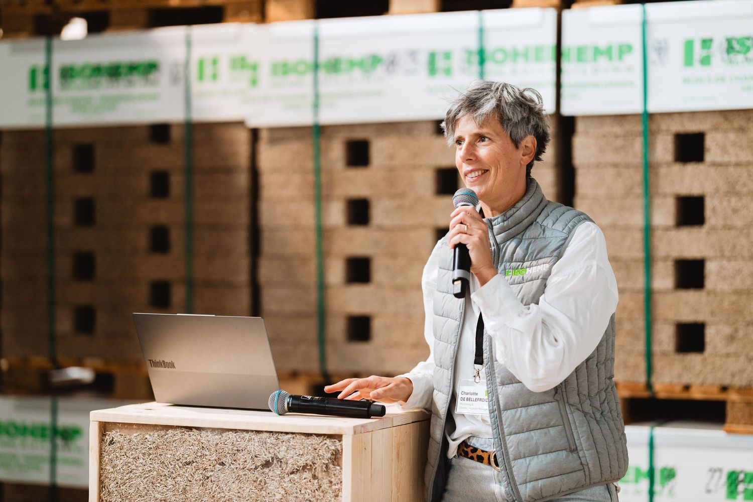 Woman speaking at podium with microphone inside hemp building materials warehouse.