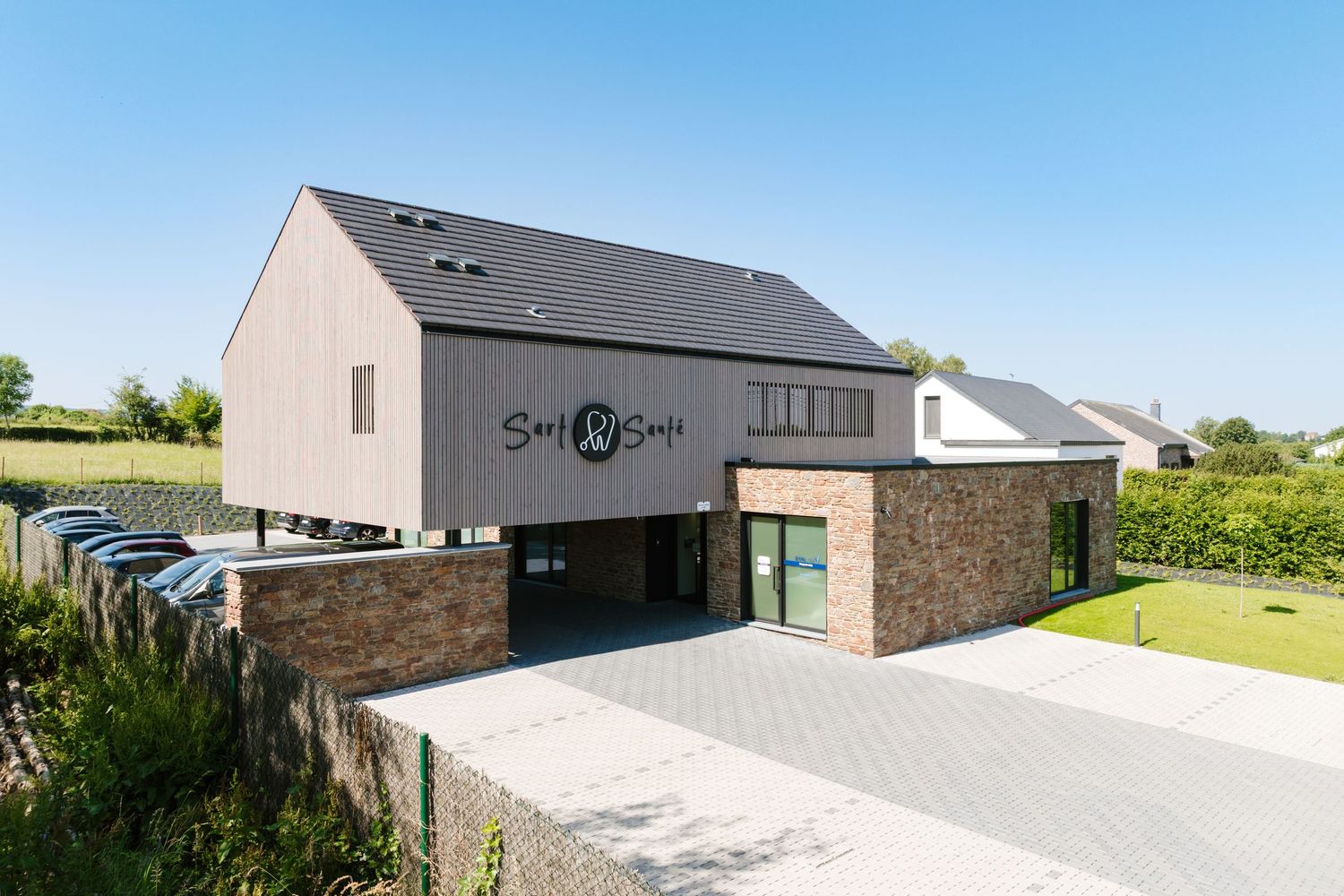 Modern brick and wood commercial building with dark roof and logo signage on a clear sunny day.