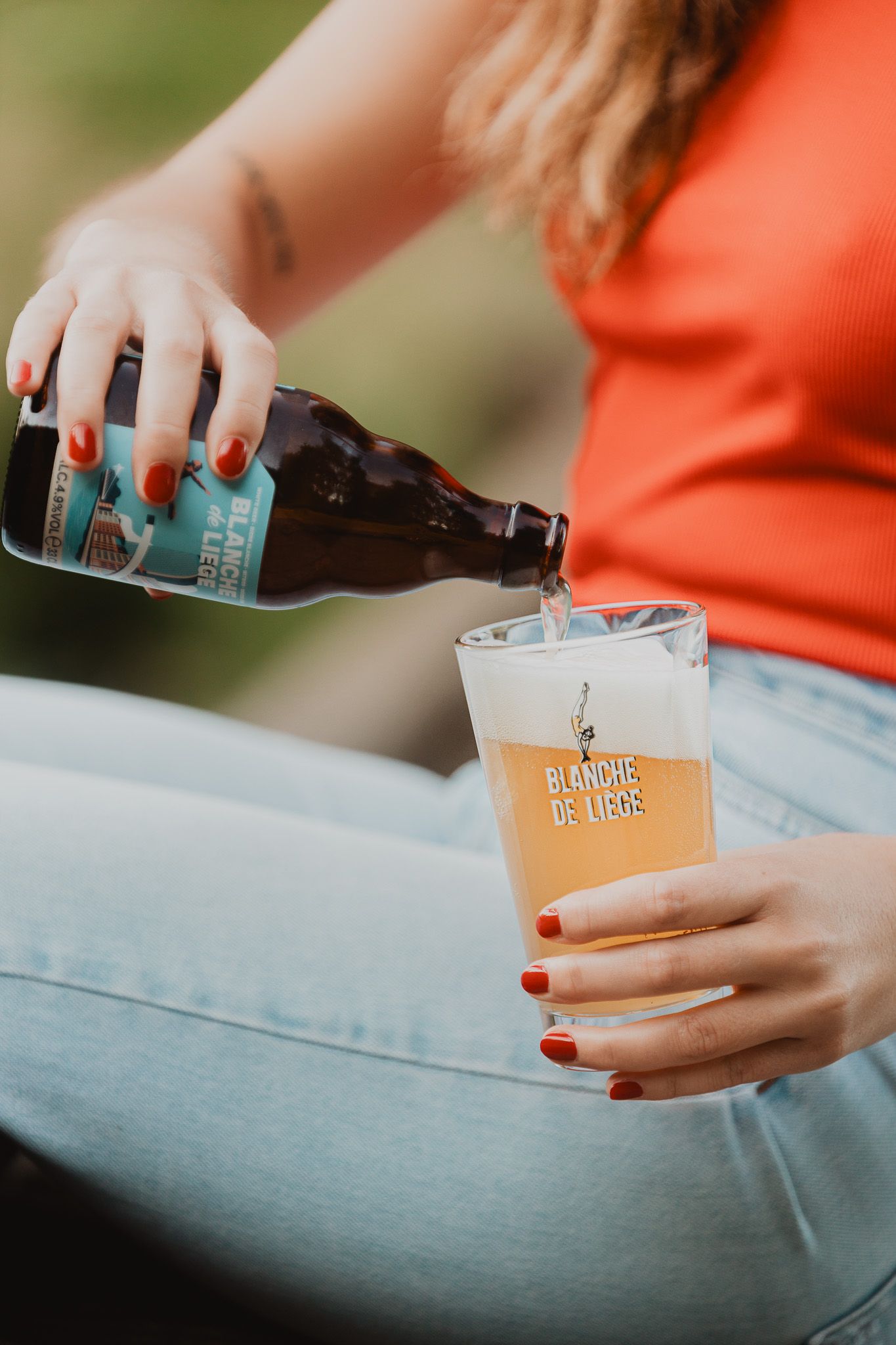 Woman pouring Blanche de Liège beer into a branded glass outdoors.