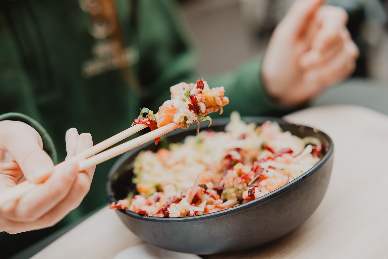 Person using chopsticks to pick up food from a colorful rice bowl at a restaurant table.