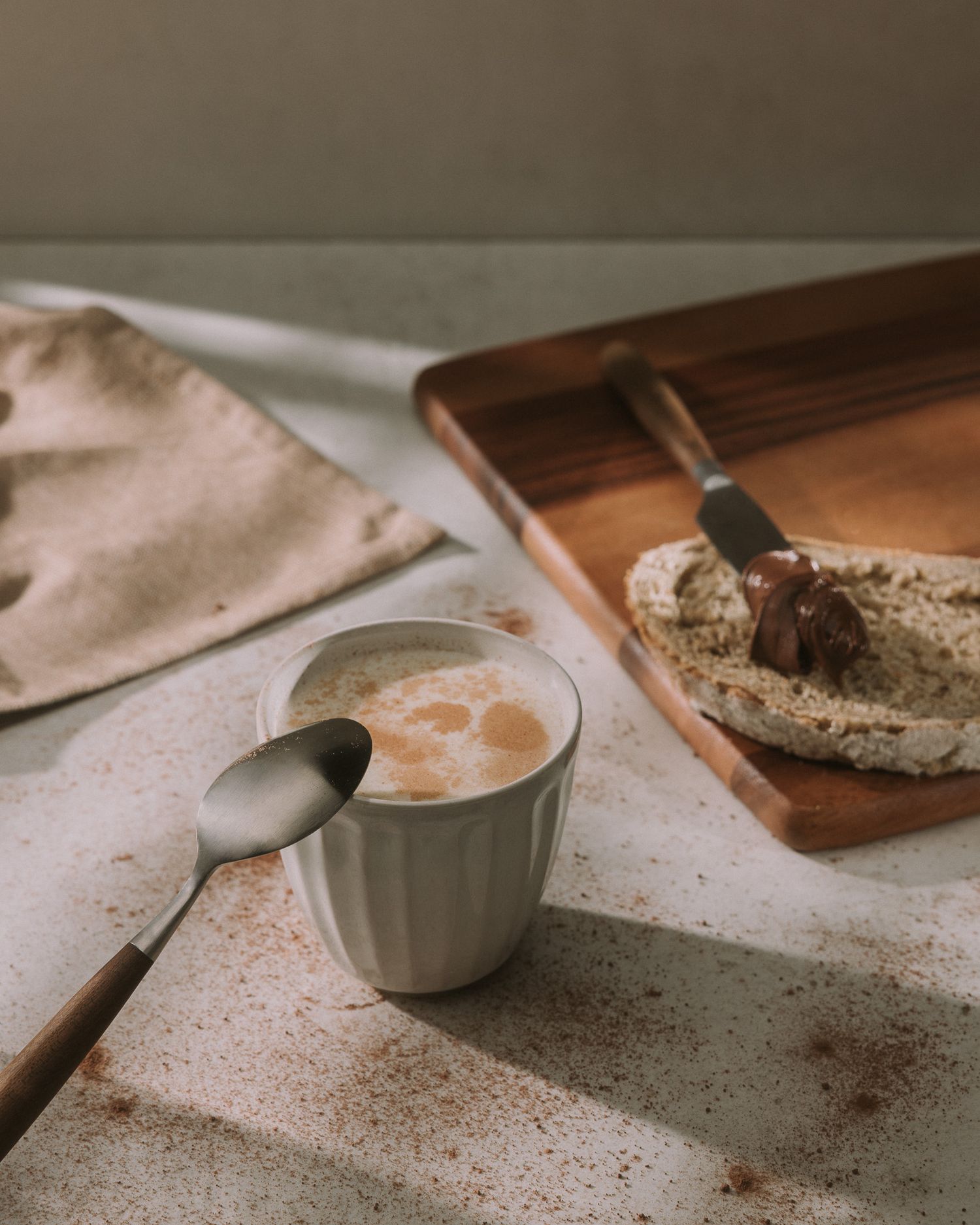 Warm styled coffee cup with spoon and chocolate spread on bread on a wooden tray.