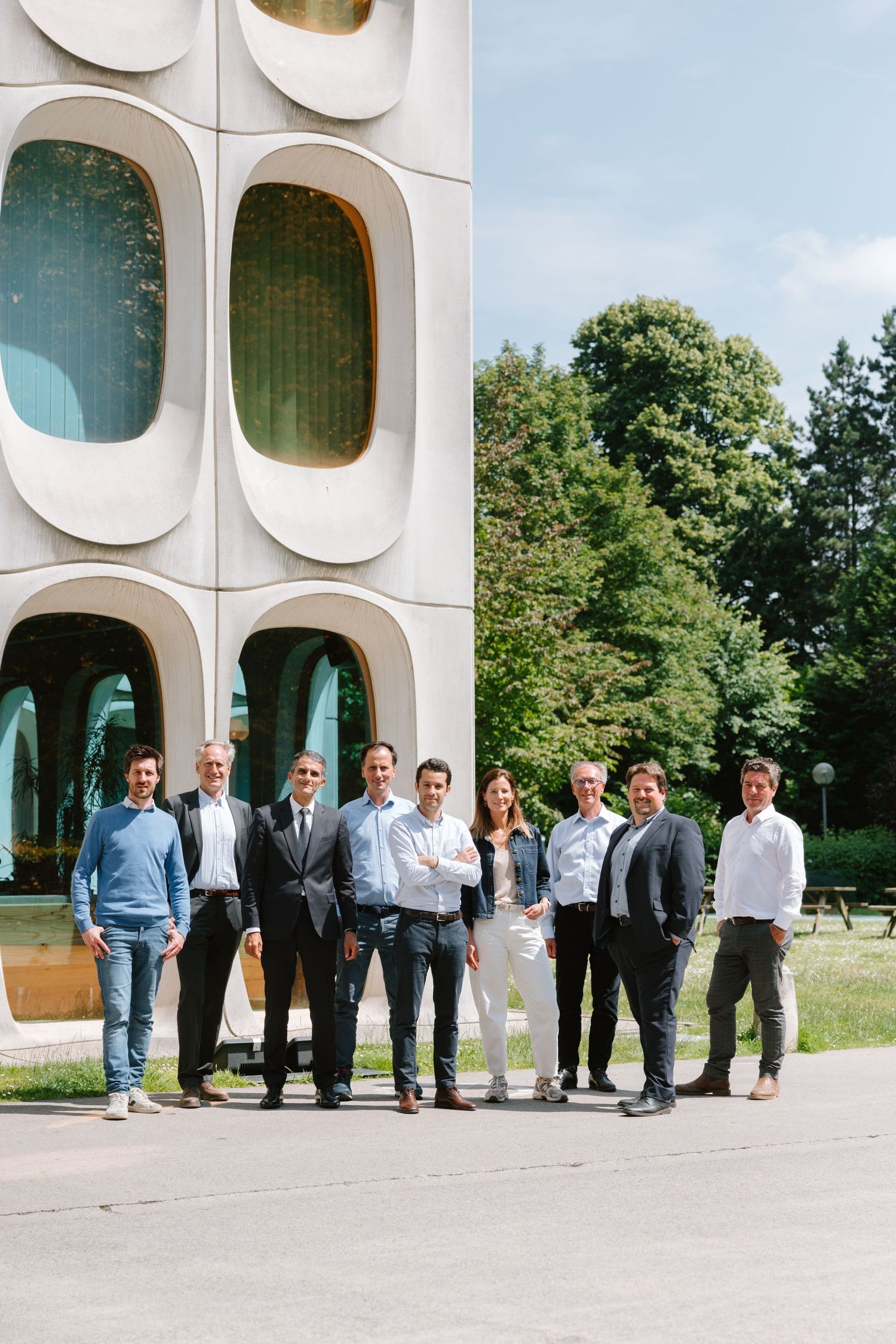 Group of business professionals posing outdoors in front of a modern architectural building on a sunny day.