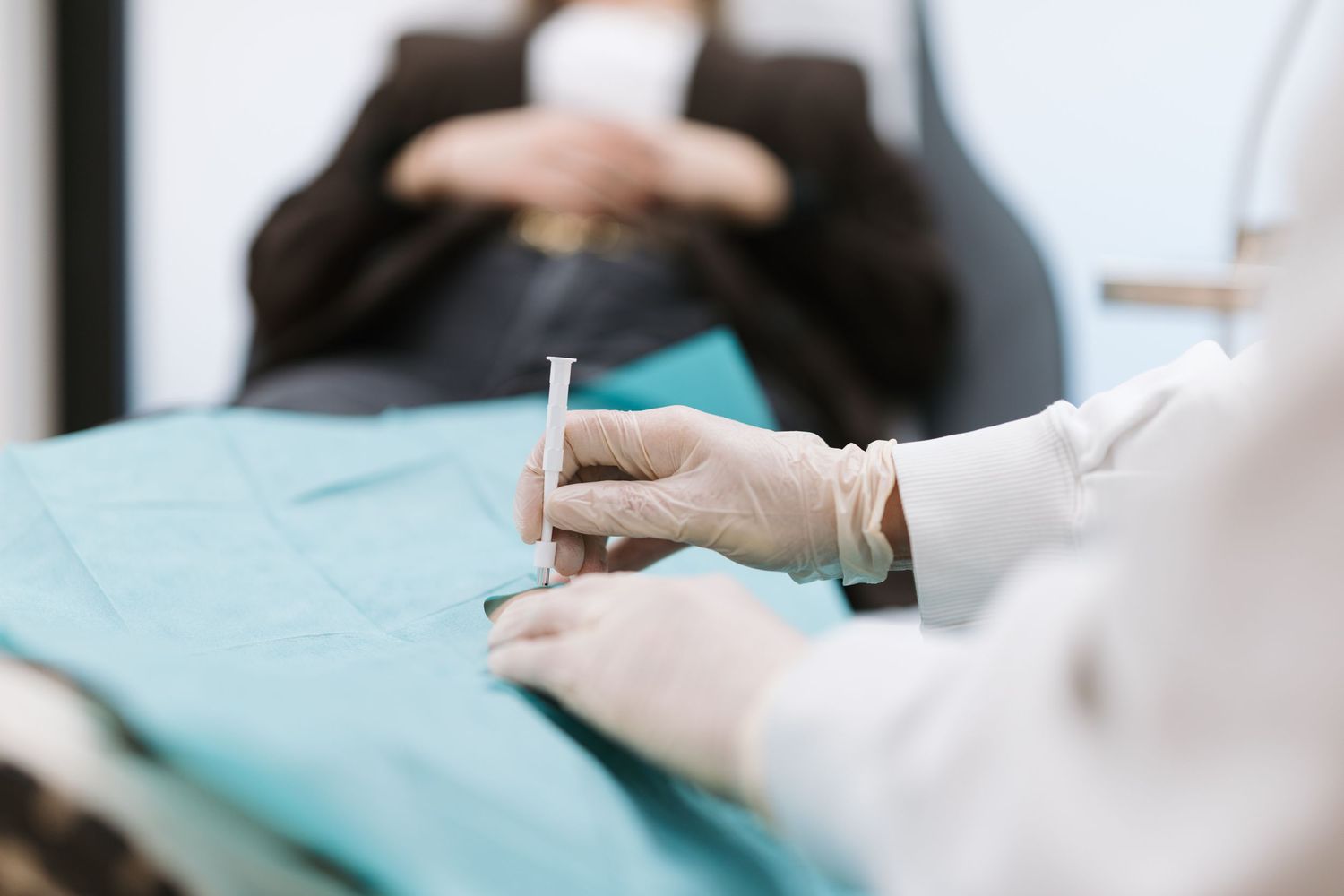 Dentist in white gloves holding a syringe over a teal surgical drape, preparing for a dental procedure.