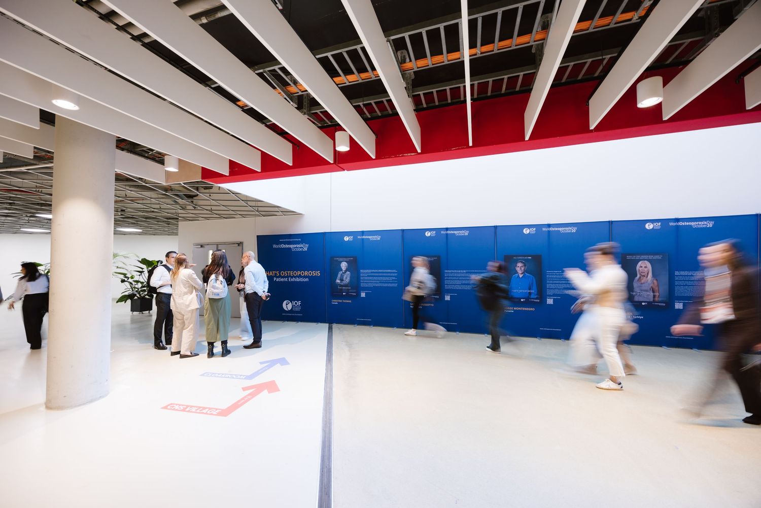 Attendees browse a blue informational display wall inside a busy modern conference center.