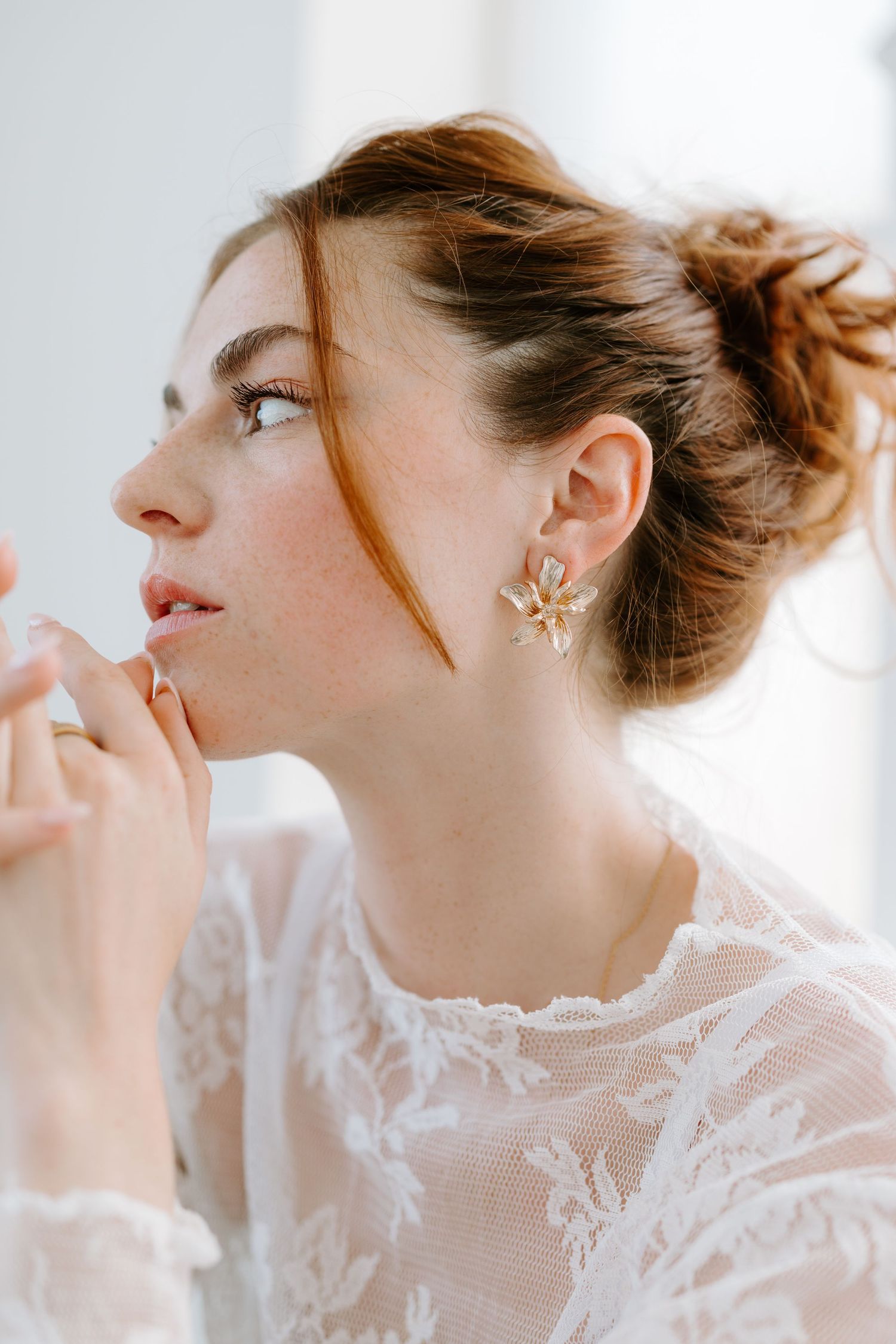 Close-up profile of a redhead woman wearing elegant gold star-shaped earrings and a white lace blouse.
