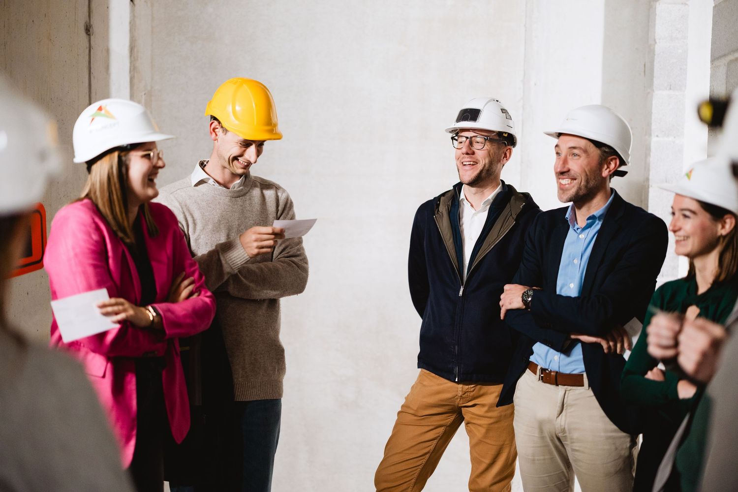 Construction team in hard hats laughing during building site walkthrough inspection.