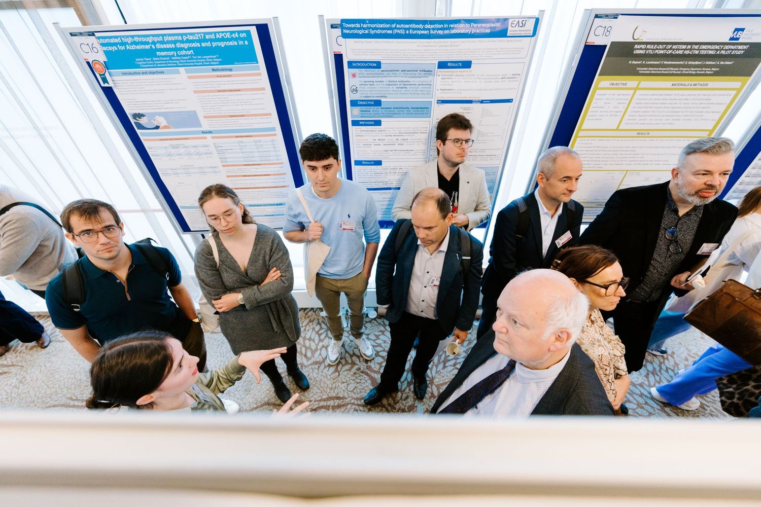 Researchers gather around academic posters at a scientific conference, engaged in discussion and presentation review.