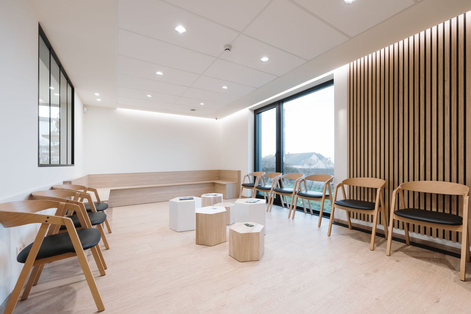 Modern minimalist waiting room with wooden chairs, slatted wall panels, and natural light from large windows.