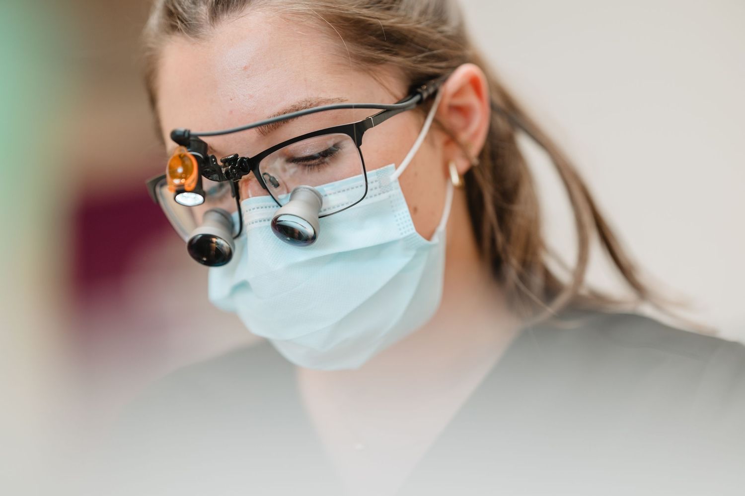 Female dentist wearing surgical mask, magnifying loupes, and headlight during a dental procedure.