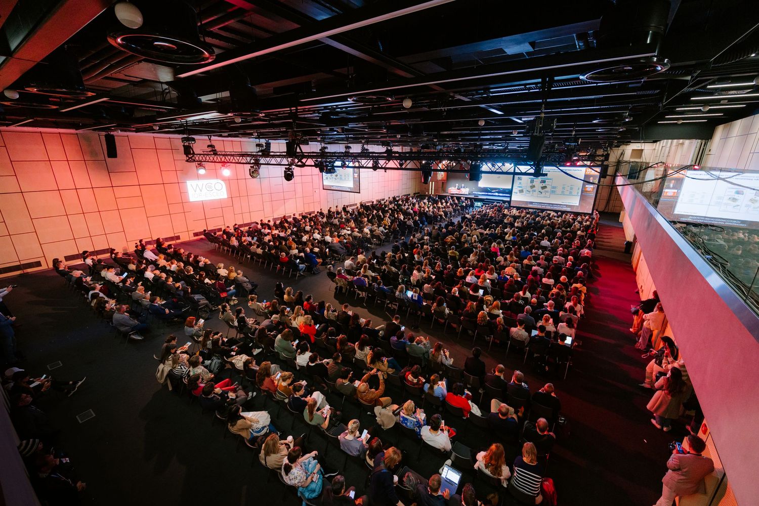Large audience seated in modern conference hall with red lighting attending a professional event.