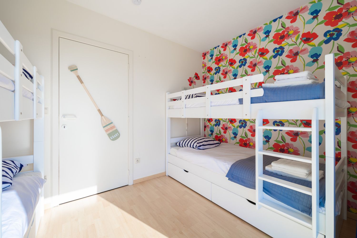 Cheerful children's bedroom with white bunk beds, floral accent wall, and light wood flooring.